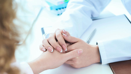 Obraz na płótnie Canvas Friendly female doctor hands holding patient hand sitting at the desk for encouragement, empathy, cheering and support while medical examination. Just hands over the table.