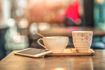 Hot coffee glass cup with smartphone on wooden table in coffee shop. Vintage tone