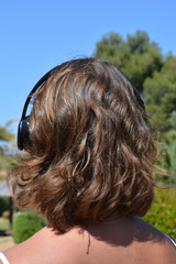portrait of a girl listening to music on wireless headphones, from behind,  outdoors