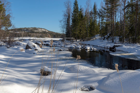 Little stream with ice and snow on both sides with reed in foreground, picture from Northern Sweden.