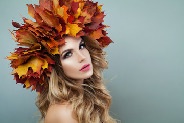 Woman face closeup. Autumn model woman with makeup, blonde hair and fall leaves