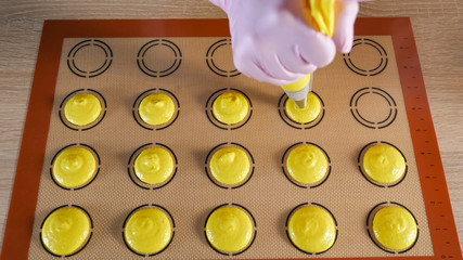Pastry chef is pouring dough from pastry bag on stencil silicone mat on the table, view from above....