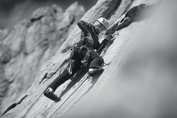 Young woman is engaged in rock climbing in the mountains. Sport climbing. Black and white.