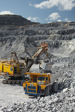 Heavy mining excavator loads rock ore into a dump-body large mining truck. Quarry equipment. Mining industry.