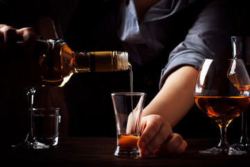 The bartender pours the golden tequila in small shot glass on the old bar counter. Vintage wooden...