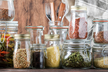 Food set. Raw cereals, pasta, groats, organic legumes and useful seeds in glass jars. Vegan source of protein and energy resources. Rustic wooden kitchen table background.