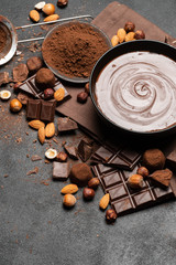 ceramic bowl of chocolate cream or melted chocolate, nuts and pieces of chocolate on dark concrete background