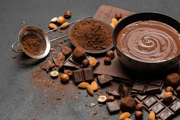 ceramic bowl of chocolate cream or melted chocolate, nuts and pieces of chocolate on dark concrete background