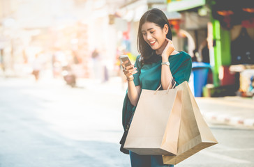 Asian women are addicted to shopping or shopaholic shopping in the old town with colorful paper shopping bags during the discount season with copy space and blur city or tourist background, Soft tone.