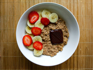 Breakfast bowl with strawberries and banana, with cereals and an ounce of dark chocolate.