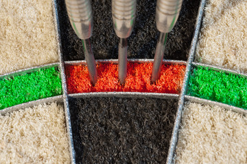 Front view on a sisal dartboard with three darts in triple twenty sector