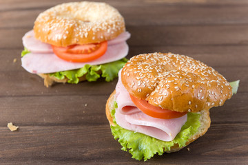 2 sandwich with ham, a leaf of lettuce, a slice of tomato on a sesame seed bun on a brown wooden background