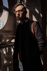 Young man posing in glasses against a urban background. Beautiful guy in stylish closes posing on parking