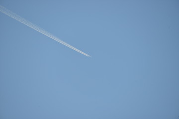 commercial aircraft at very high altitude with white contrail on cloudless blue sky