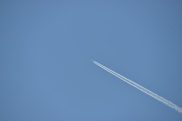 commercial aircraft at very high altitude with white contrail on cloudless blue sky