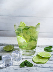 Mojito cocktail with slices of lime and mint leaves in highball glass on a wood table. White background.
