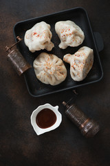 Cast-iron serving tray with georgian khinkali dumplings, above view on a dark brown metal background, vertical shot