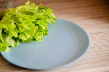 Fresh green lettuce leaves on a blue dish . Glettuce on a plate brown wooden table.