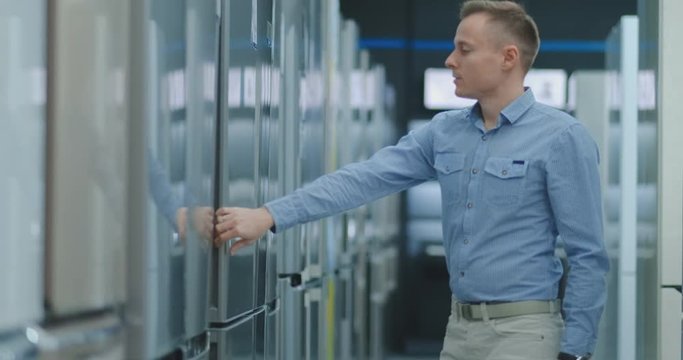 A man opens the door of the washing machine inspect the design and quality before buying in a consumer electronics store. Read the information on the price tag and characteristics