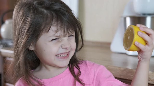 Kid wrinkles from lemon. Cute little girl winces looking at the lemon in her hand.