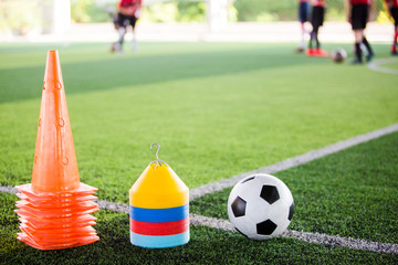 football and marker cones are soccer training equipment on green artificial turf with blurry of soccer players training. Soccer Academy.