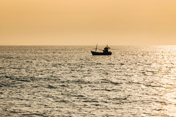 Obraz premium fishing boat in ocean with golden sunshine at sunrise