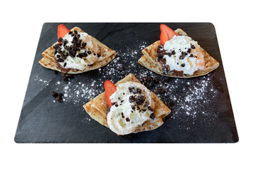 pancakes with strawberries chocolate and cream on a black board isolated on white background