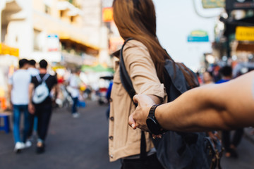 Young girlfriend holding hand of boyfriend. Tourist backpacker couple walking in street market together in Bangkok, Thailand. Follow me concept