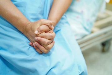 Asian senior or elderly old lady woman patient hold her hand with hope while sitting on bed in nursing hospital ward : healthy strong medical concept 