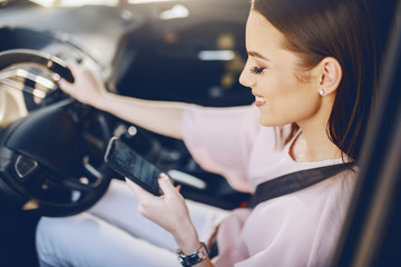 Fototapeta na wymiar Attractive young Caucasian brunette with toothy smile and dressed elegant driving car and looking at smart phone.