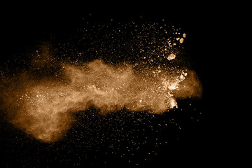 Brown particles splattered on black background. Brown dust splashing.