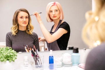 Brow and make up artist shaping and coloring eyebrows of her woman client in salon. Procedure in process. Space for text