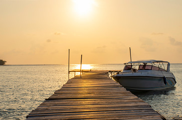 Naklejka premium Speed boats moored at the wooden bridge in the sea and Golden reflections of the Sun