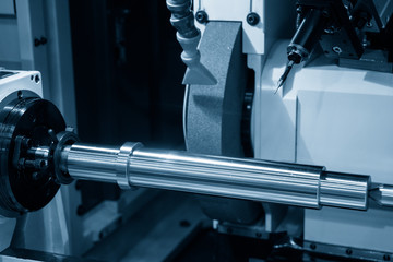 The cylindrical grinding machine in the light blue scene with the steel shaft.The automotive part manufacturing process.