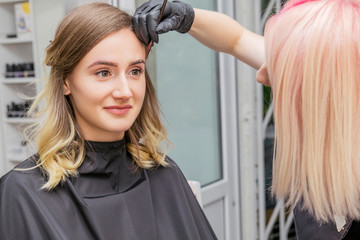 Fototapeta premium Brow and make up artist shaping and coloring eyebrows of her woman client in salon. Procedure in process. Space for text