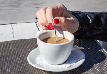 female hand stirring  coffee with a teaspoon in an outdoor cafe