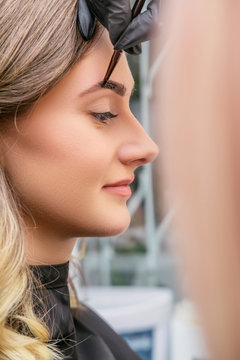 Brow and make up artist shaping and coloring eyebrows of her woman client in salon. Procedure in process. Space for text