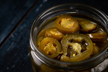 Homemade spicy jalapeno peppers marinated and sliced in a glass bowl on a dark wooden background