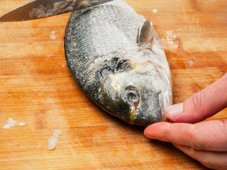 Fishmonger holding fish with his fingers on a wooden table. Sea-bream descaling.