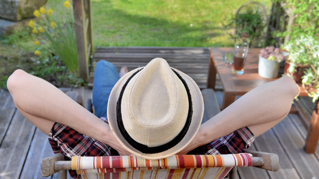 Young Man Seen Back Wearing A Hat And Relaxing On A Terrace In A Garden