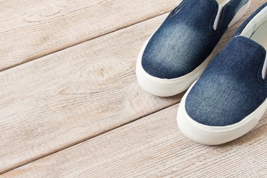 Denim slip-on shoes on wooden background. Top view.