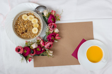 Breakfast in bed with muesli, fruit and orange juice with flowers and a card