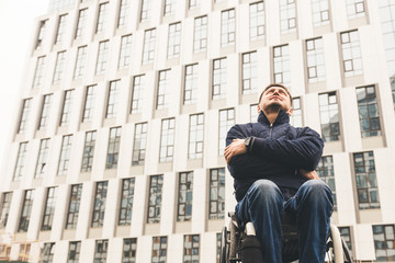 Young man in a wheelchair against the backdrop of a modern high-rise building.