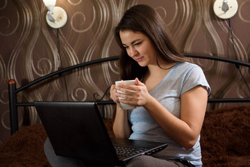 Casual beautiful woman working on a laptop sitting on the bed i