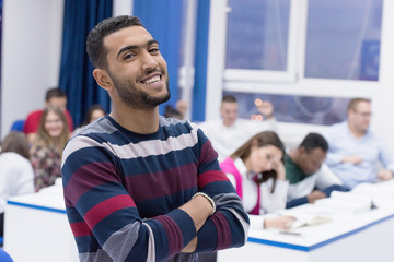 Students life on the campus.Portrait of male college student smiling and looking at camera during class in the classroom. University male african american student standing  in classroom.