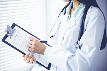 Doctor woman working with medication history records form while standing near window in clinic. Medicine and health care concept. Green is main color