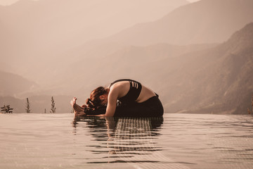 Beautiful Asian woman practice yoga sitting forward fold pose on the pool above the Mountain peak...