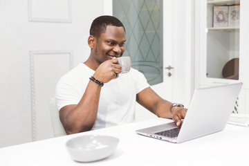 Young African American businessman working on a laptop in the kitchen in a modern interior.