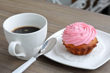 Cream cake and cup of coffee. Cake lies on a saucer. Near a coffee spoon.
