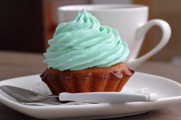 Cream cake and cup of coffee. Cake lies on a saucer. Near a coffee spoon.